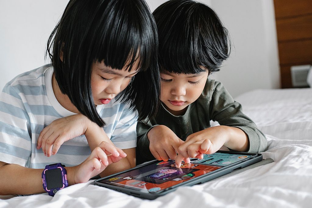 Zwei Kinder beschäftigen sich mit einem Tablet.