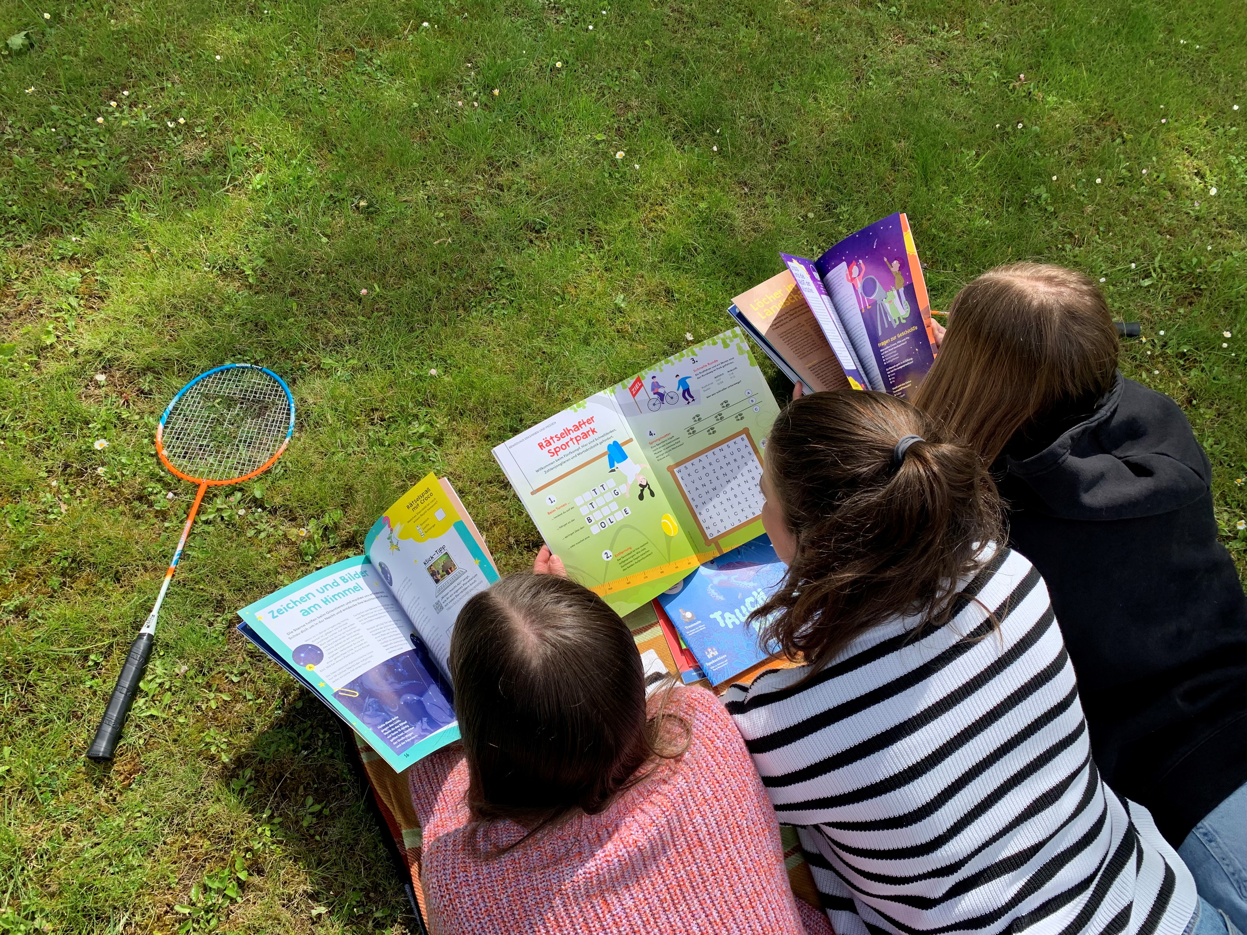 Auf einer Picknickdecke im Park liegen drei Mädchen und lesen in verschiedenen Zeitschriften