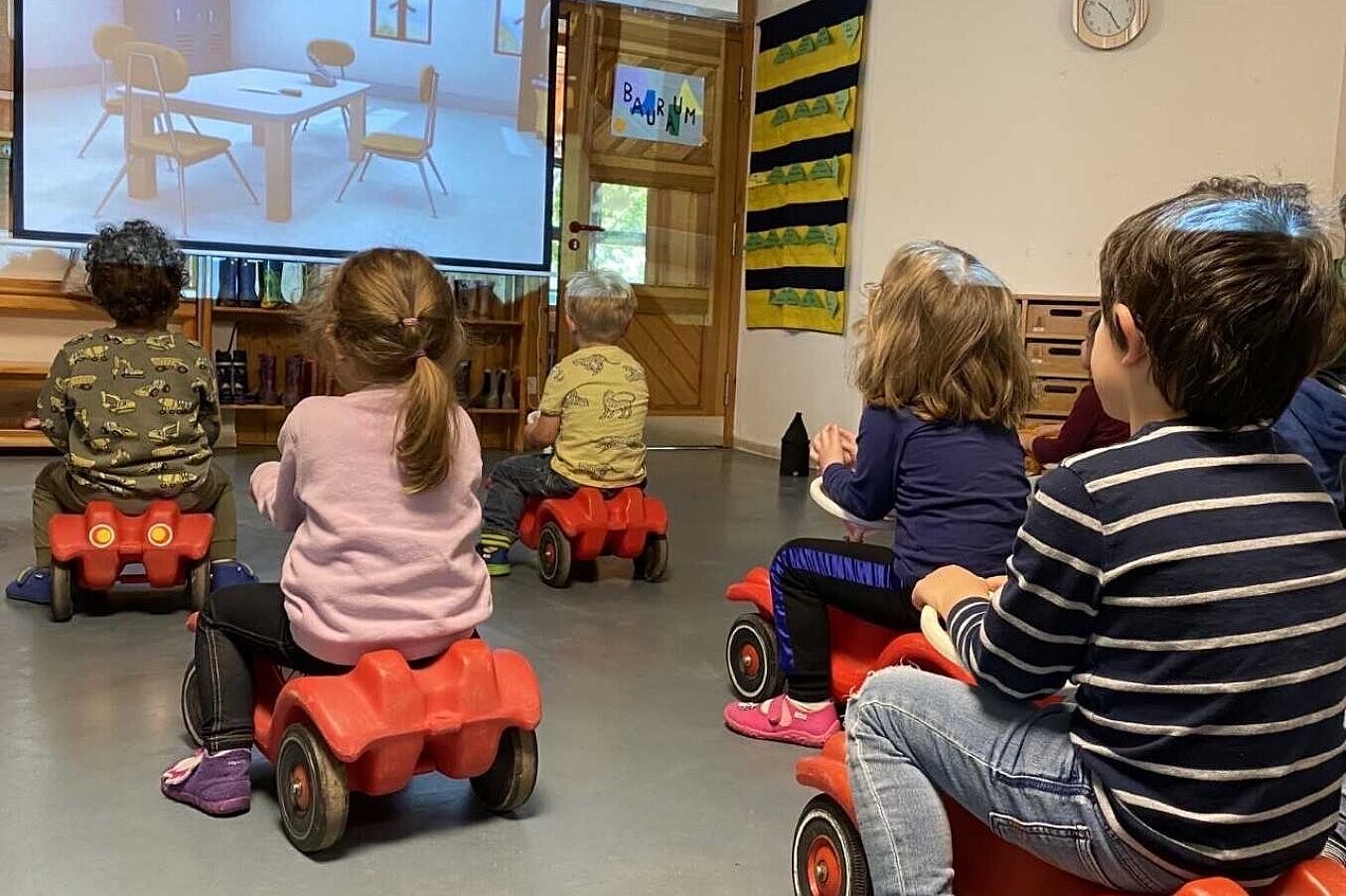 Kinder auf Bobbycars schauen auf die Projektion eines Beamers