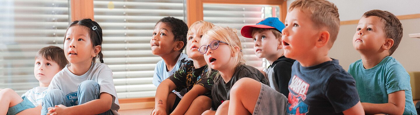 Kita_Portal_Krippe_Kita_Header Kinder sitzen auf dem Boden und hören beim Vorlesen zu